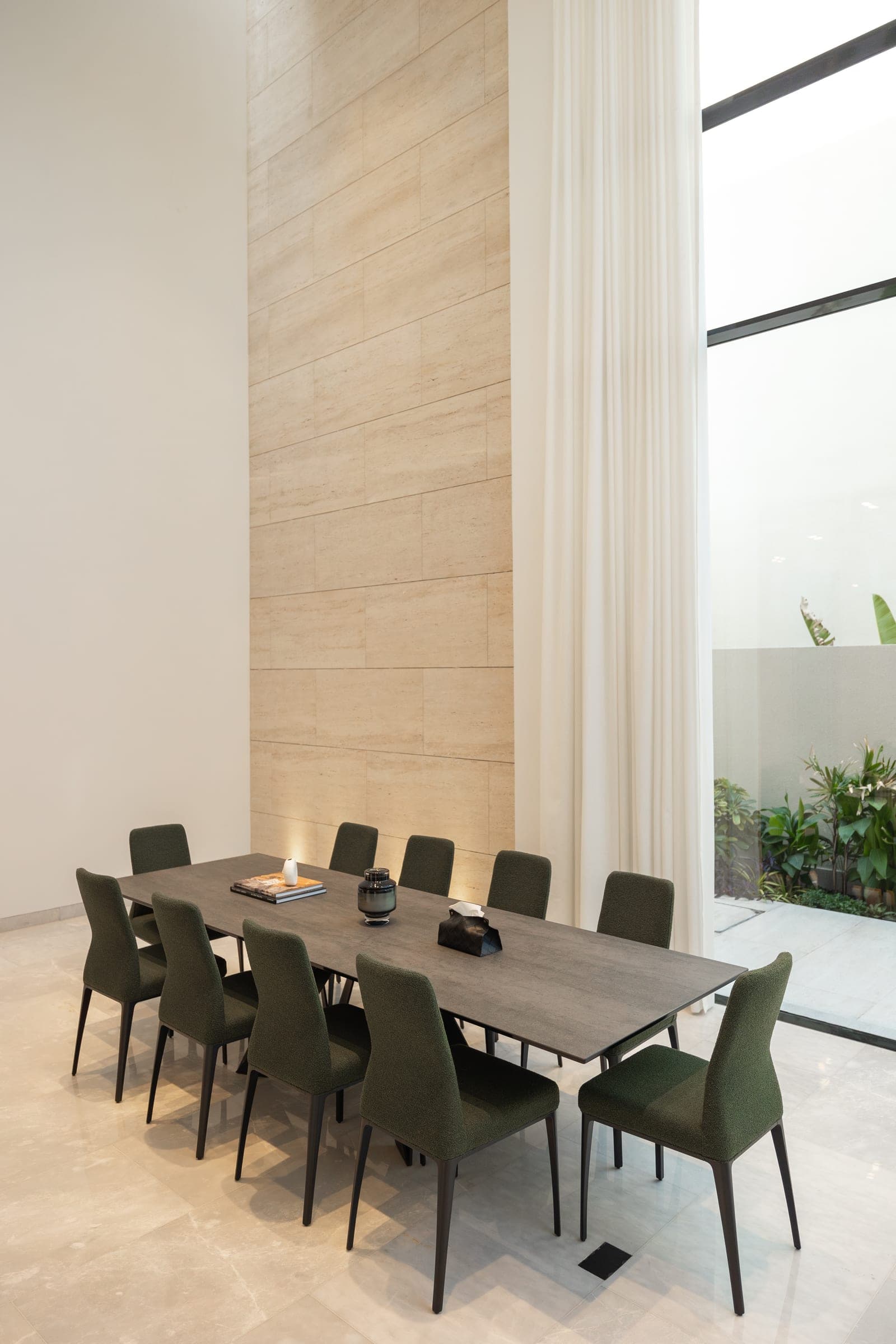 Dining table with green chairs beneath a double-height travertine wall at The Cube 61, a LKYOOB commission