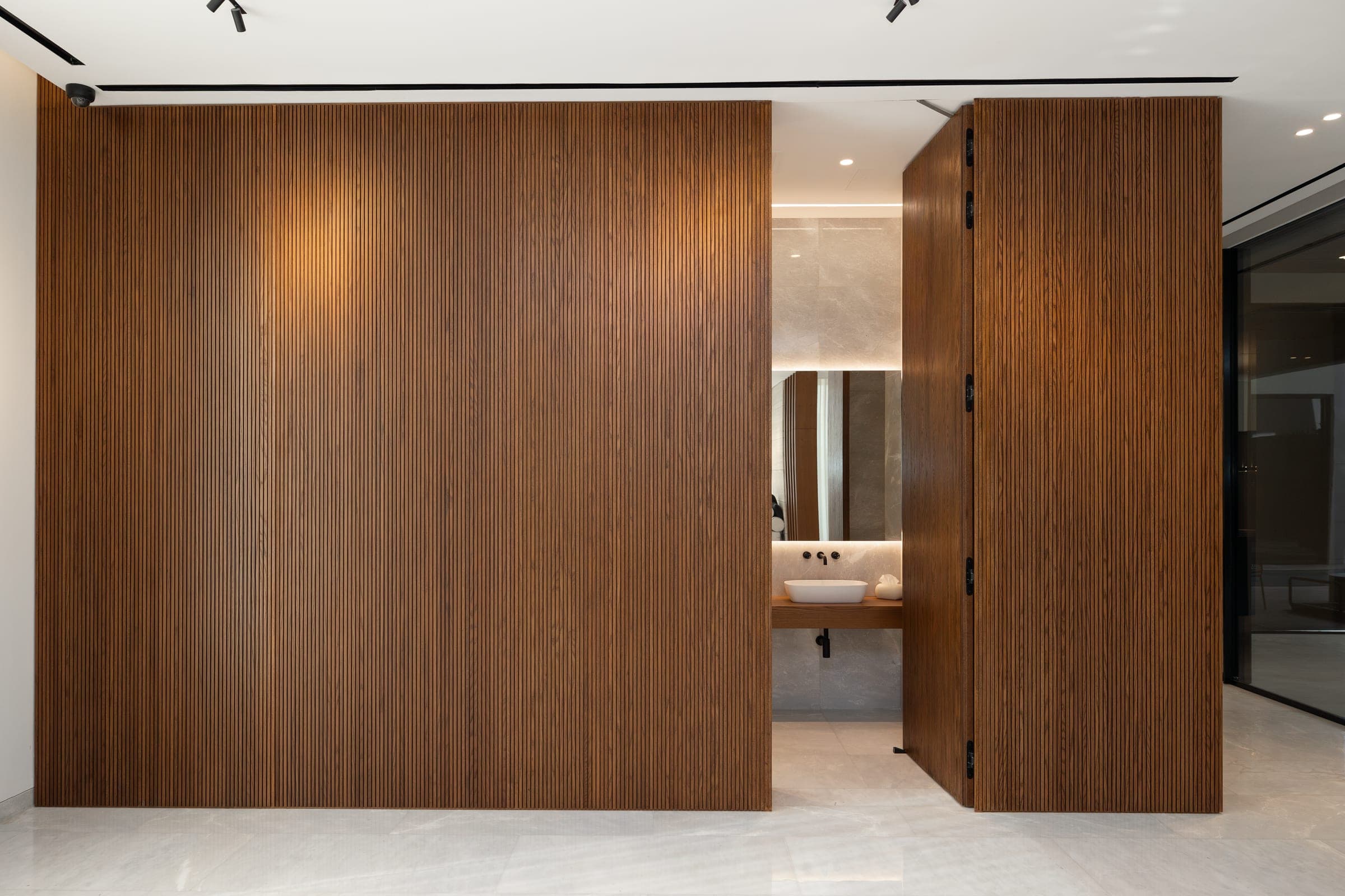 Fluted walnut doors opening to a bathroom with a stone basin at The Cube 61, a LKYOOB commission