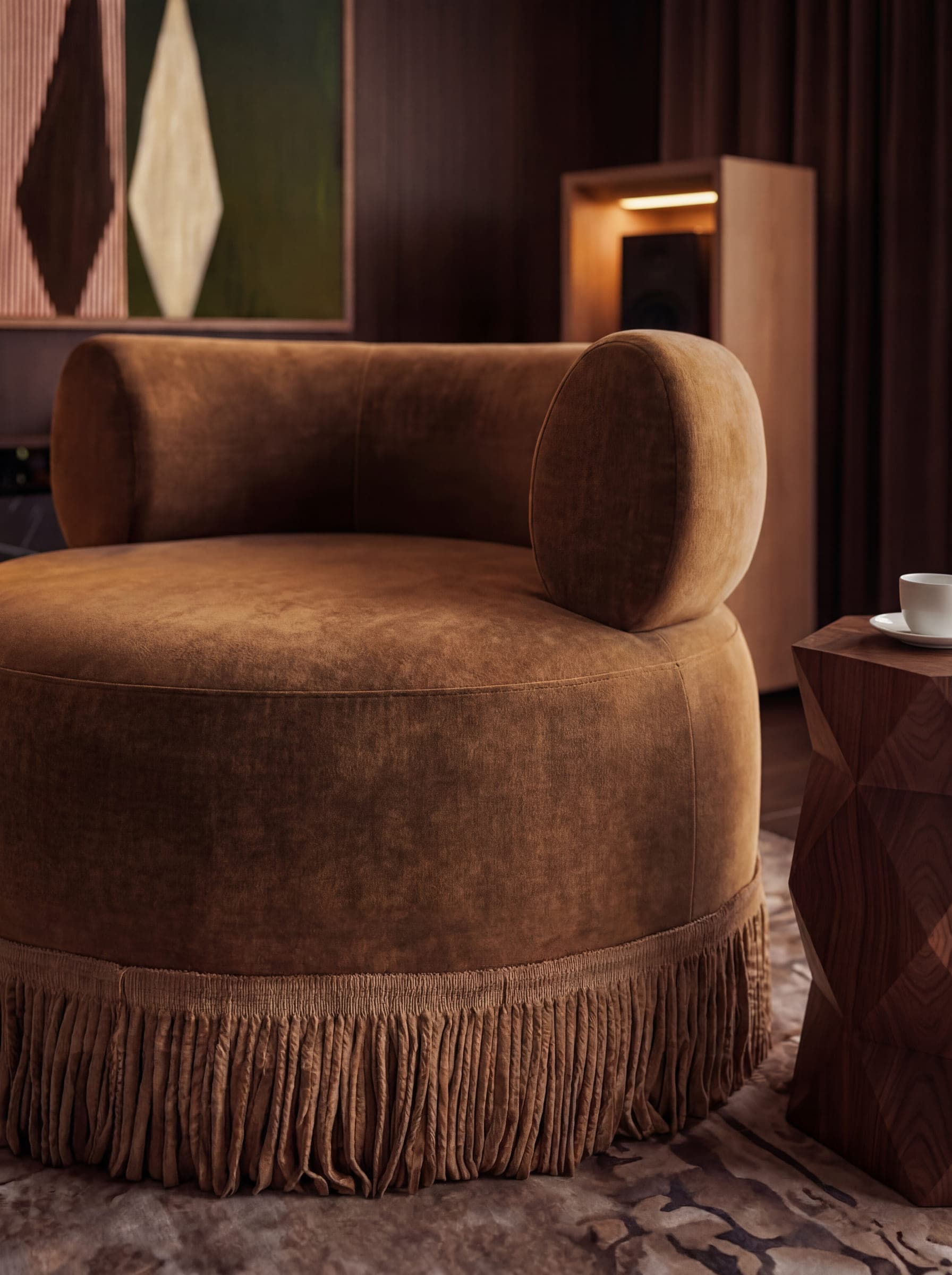 The fringed skirt and rolled back of a brown velvet armchair in warm lamplight — material study by LKYOOB