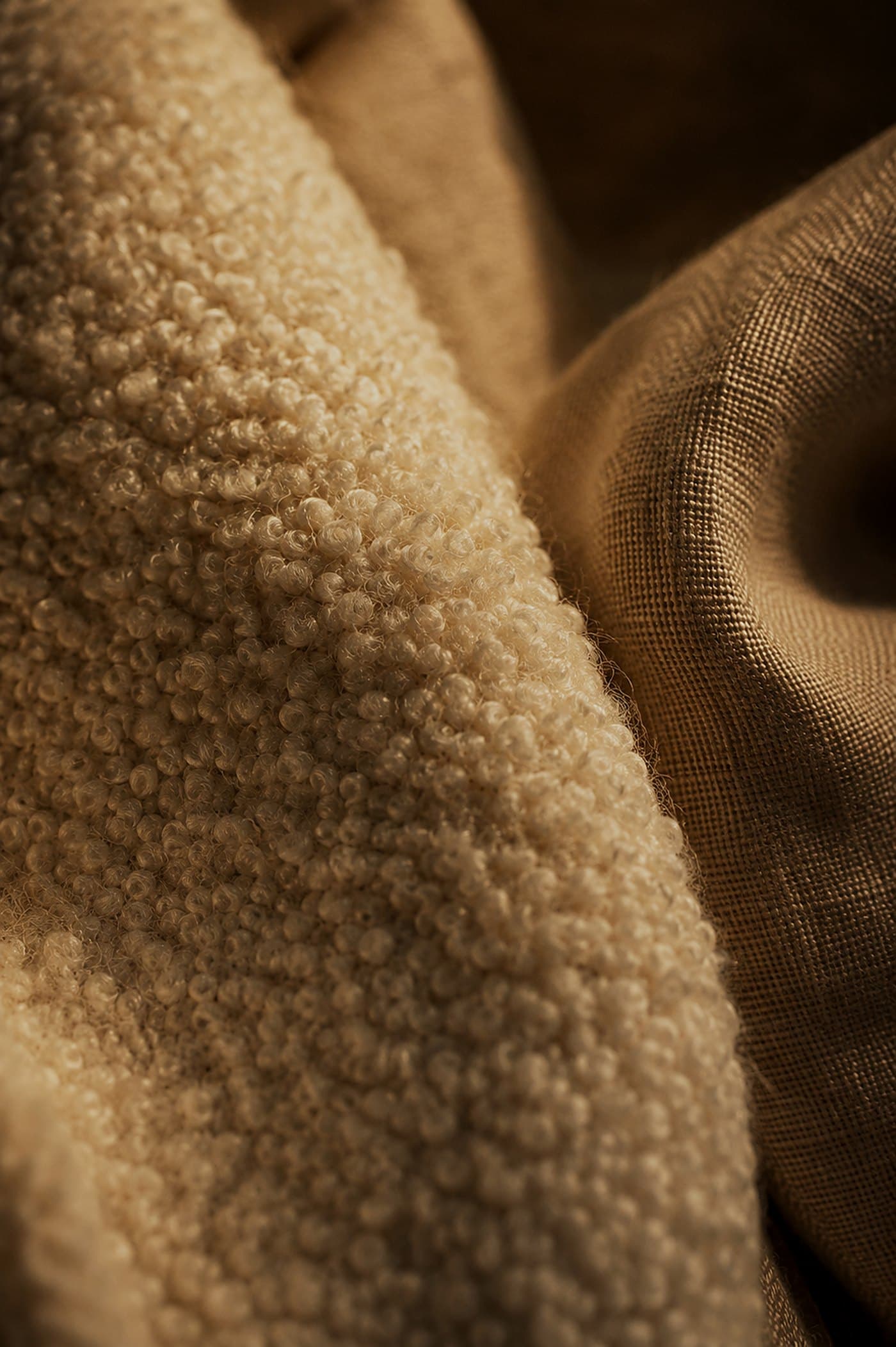 Cream bouclé wool texture draping over woven linen in warm raking light — material study by LKYOOB
