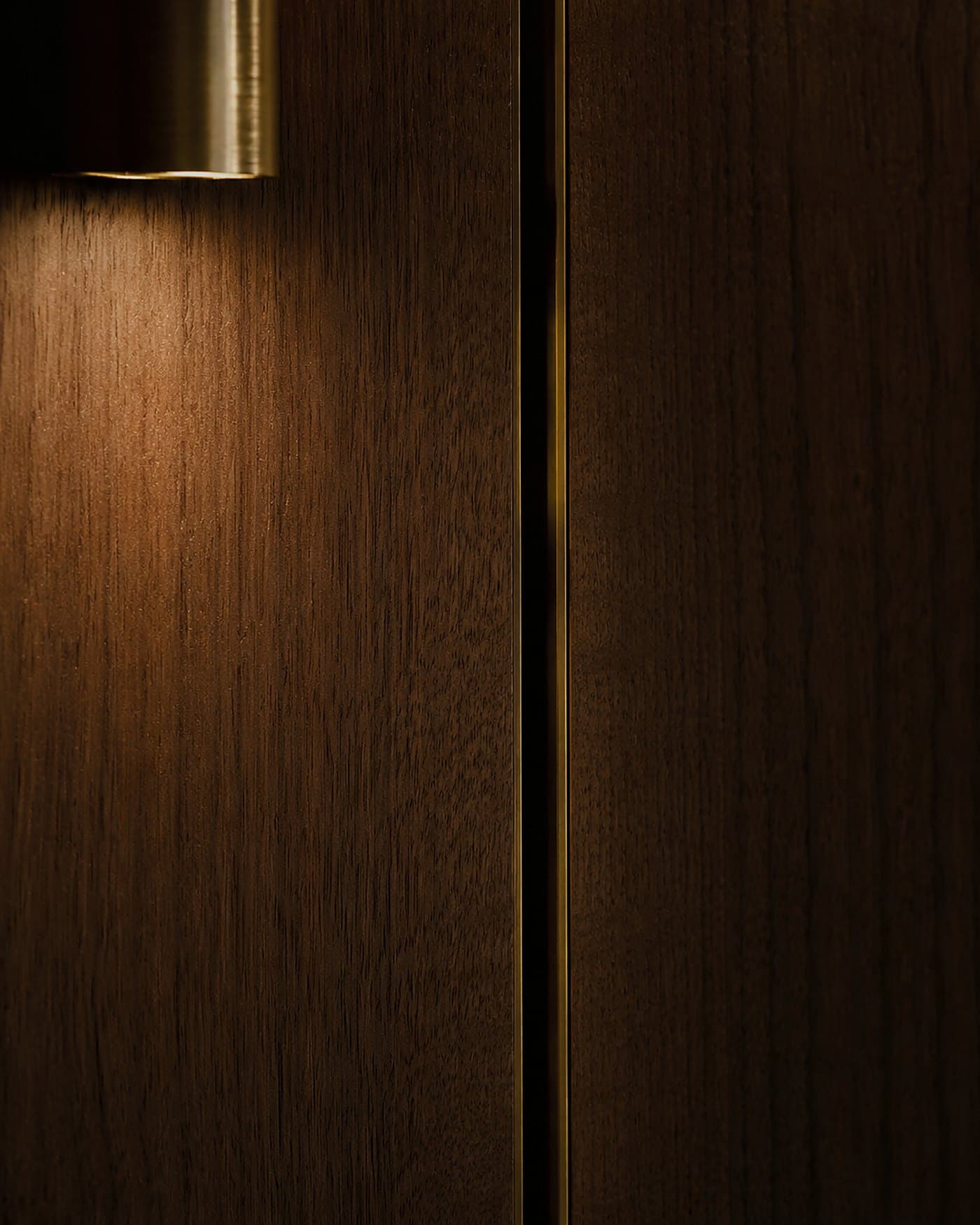 Rift-sawn American black walnut panelling with a glowing brass shadow-gap reveal under warm sconce light — material study by LKYOOB