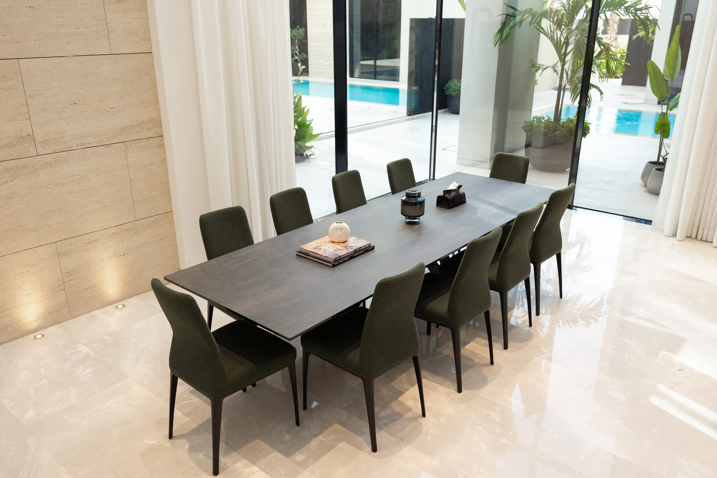 Dining room with a long dark table and a view through glazing to the pool, at The Travertine Villas, a LKYOOB commission