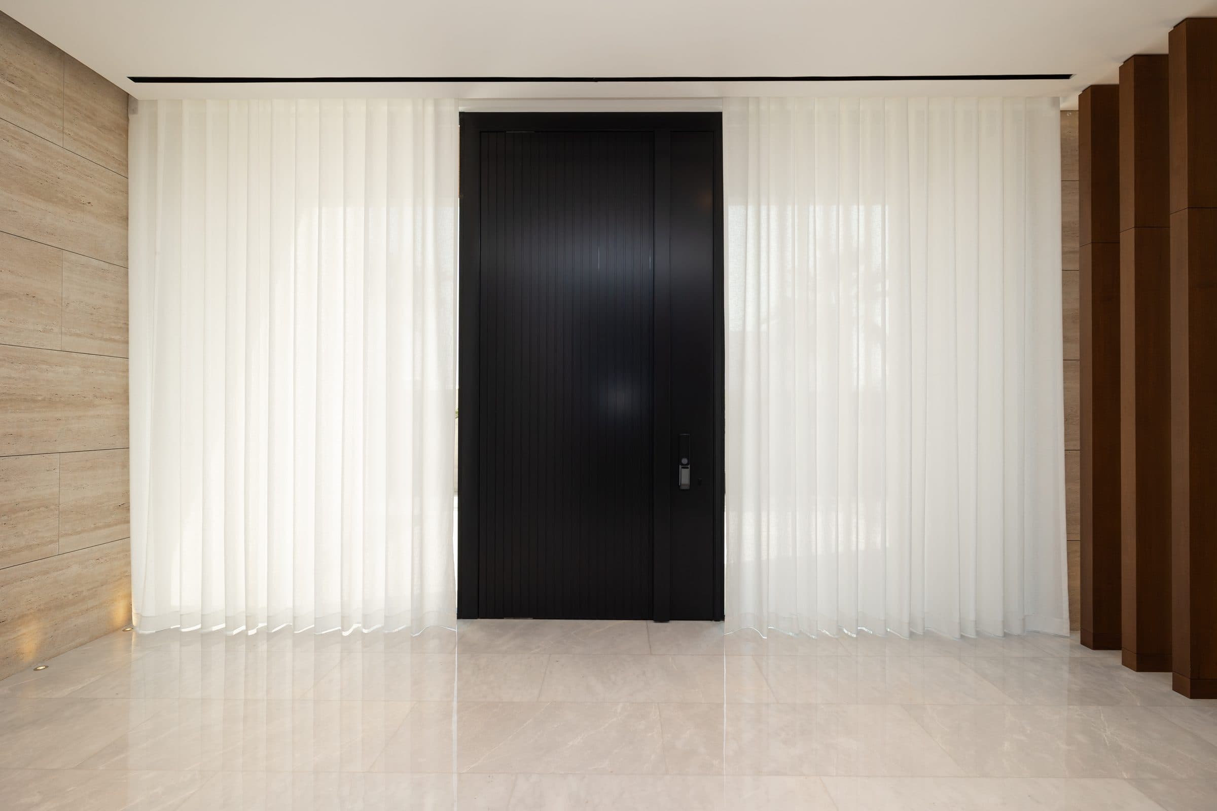 Entrance hall with a full-height dark pivot door and sheer curtains at The Travertine Villas, a LKYOOB commission