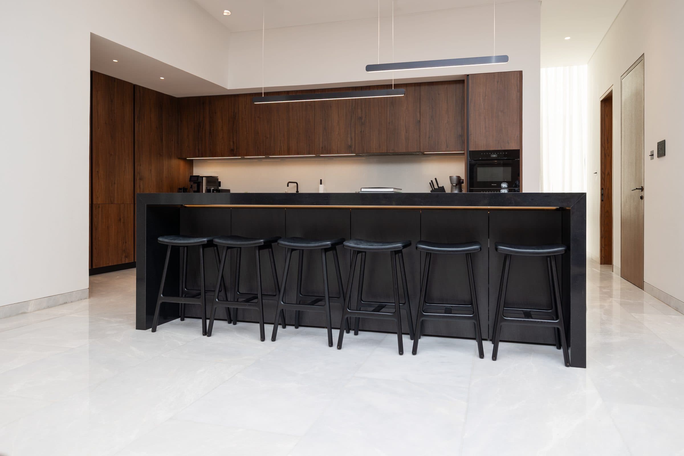 Kitchen with a black stone island, bar seating and dark walnut joinery at The Travertine Villas, a LKYOOB commission