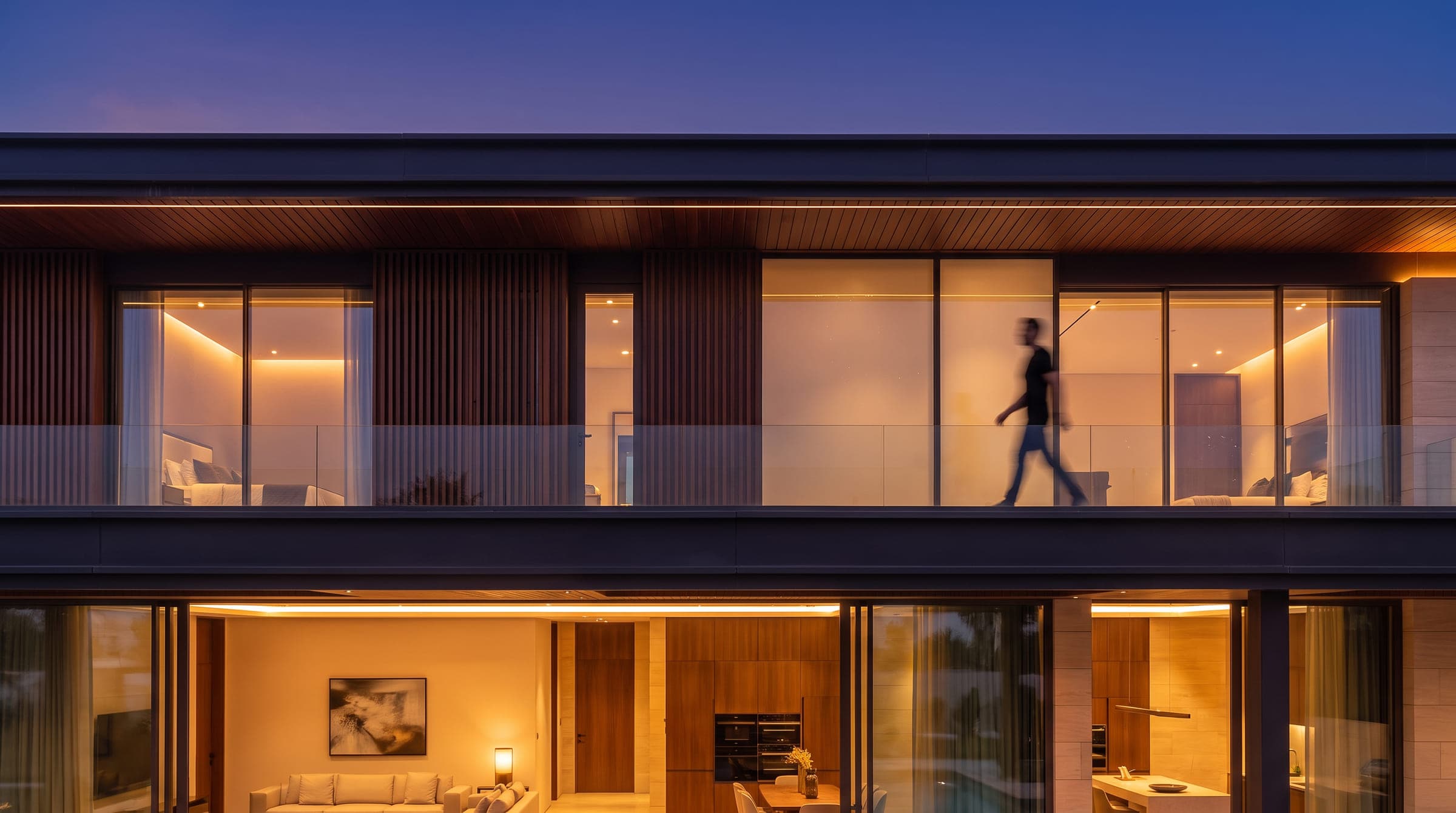 Design visualisation of the garden elevation at night, the upper bedrooms behind a glass balcony over the lit living floor, by LKYOOB